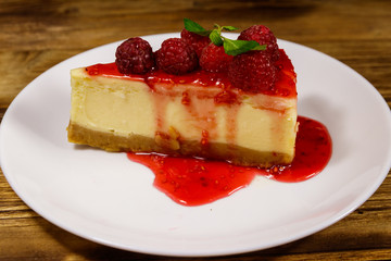 Piece of tasty New York cheesecake with raspberries and raspberry jam in a white plate on wooden table