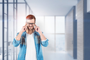 Man in glasses covering ears in office lobby