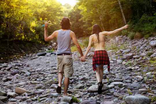 Rear view of young couple walking along rocky riverbank in forest 