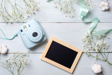 Photo camera and picture frame on blue wooden table. Spring minimal flowers frame, pastel colors, flat lay style, top view. Beauty technology concept, fashion blogger photo device. 