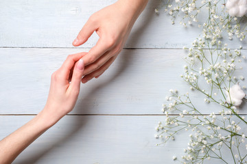 Young couple hand on blue wooden table with flowers . Bonding concept, flat lay, above view