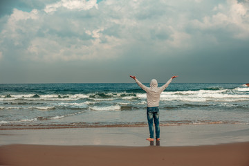 Man on the beach. The man with his hands in the air is standing barefoot on the beach and looking at the sea