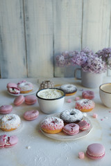 Cup of cappuccino, fresh colorful donuts, strawberry macarons and bouquet of lilac on white marble table