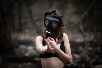 Anonymous woman in black clothes and gas mask standing in amazing spooky forest