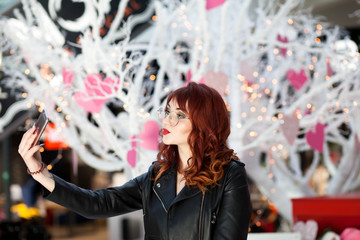 Stylish lady making selfie in the mall. Girl is photographed near the Valentine's Day scenery