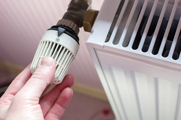 Hand of a man turning the radiator thermostat to a minimum with the coming of spring and warming in the apartment on the background wall with striped wallpaper.