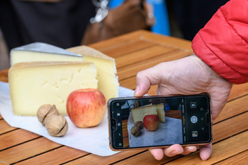 Hand of a man photographing a cheese with apple and nuts arrangement, using a mobile phone