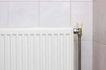 Heating radiator temperature controller in the apartment, against the background of a a tiled wall.