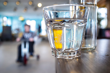 Glass of water stands on the edge of a wooden table, carelessly left with the possibility of falling, on a blurred background a child riding a bicycle. Safety concept.