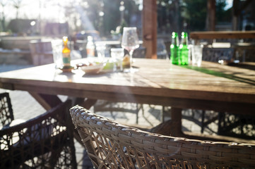 Dirty bottles, glasses, a wineglass and plates remained after eating and drinking drinks on a wooden table in the rays of the bright sun, in a street cafe.