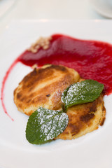 Cheesecakes or cottage cheese pancakes are decorated with icing sugar, mint and jam in a plate closeup. Healthy and diet breakfast.