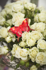 A bouquet of white roses in a vintage vase. Decorative butterfly made by hands sits on the flowers. Home decor. Flowers for the holiday.
