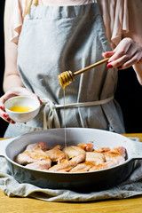 The chef's hands marinate raw chicken wings in honey. Side view