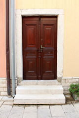 Obraz na płótnie Canvas New hardwood family house entrance doors with decorative details and baroque style door handle mounted on stone frame wall next to two gutter pipes and stone steps in front on warm sunny day