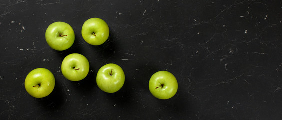 Top down view, green apples on dark marble board. Healthy food with fruit banner, space for text on right.