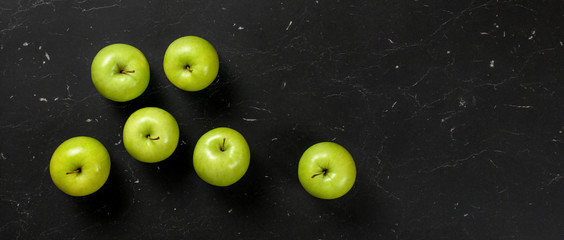 Top down view, green apples on dark marble board. Healthy food with fruit banner, space for text on...