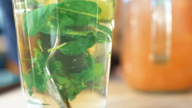 Stir tea in glass with spoon. Fresh hot tea with mint and lime inside. Close up 4k slow motion footage.