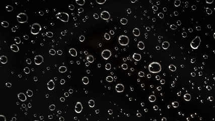 Closeup - rain water drops behind glass look like bubbles in black liquid. Abstract wet background.