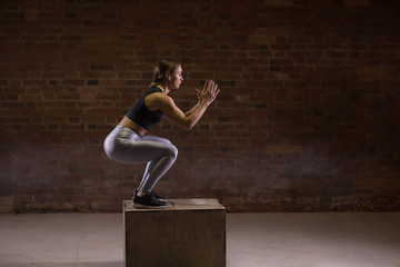 Fit young caucasian woman is performing box jumping at a cross fit style gym. Female athlete is doing box jumps at gym in fitness centre
