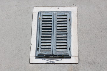 Old blue wooden window blinds with dilapidated cracked faded paint and metal hinges mounted on grey...