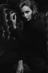 Fototapeta premium Lovely young model with long hair wearing jacket posing on a vintage sofa. Black and white toning
