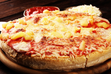 Delicious pizza with pineapple, ham slice, bacon slice, mozzarella cheese, pizza sauce on rustic background for fast food and ready to eat concept