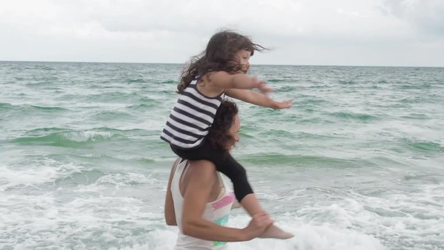 Circling the child. Fun with mom on vacation. A little girl sits on her mother's shoulders, her mother circles her on the seashore.