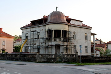 Old villa under complete reconstruction from outer facade to inner rooms with scaffolding and construction material located on crossroads surrounded with family houses on warm sunny day at sunset
