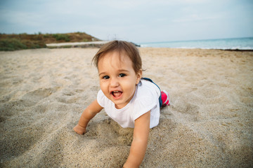 Small baby, little girl in white t-shirt creeping, playing in sand at the beach