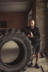 Obraz na płótnie Canvas Strong athlete turning over huge tire in CrossFit studio with minimalistic brick walls interior. This is an exercise that simulates simultaneously deadlift, sharp rise from the knees and pushing up.