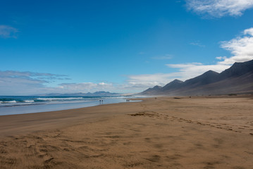 Fototapeta na wymiar Cofete beach, Jandia peninsula, Fuerteventura, Canary Islands. Footprints on the sand and high mountains on the shore. 