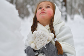 little girl breathing warms frozen hands in mittens. Red nose and cheeks