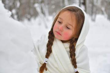 little girl in shawls and mittens in winter forest, looking for snowdrops. Portrait