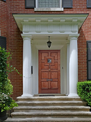 portico entrance of brick house with large white columns, elegant wooden door and stone steps
