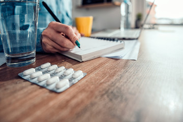 Medical pills and glass of water by the woman writing notes