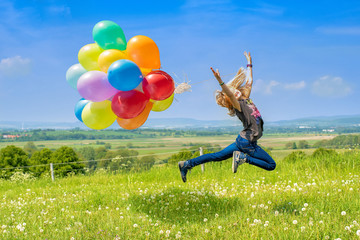 Glückliches Mädchen spring mit bunten Luftballons über eine grüne Wiese