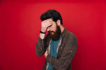 Close up portrait of disappointed stressed bearded young man in with closed eyes over red background