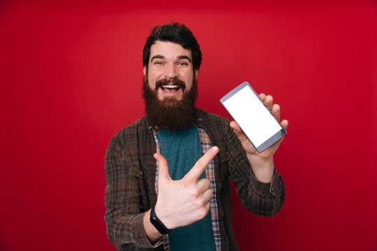 Portrait of a confident young bearded man, showing blank screen mobile phone, pointing finger