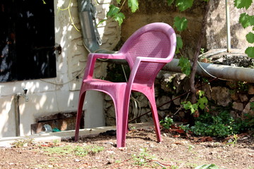 Plastic backyard chair with faded dark pink color surrounded with traditional stone wall and gutter...