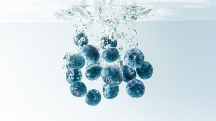 Bunch of blueberries sinking in crystal clear water after splashing into surface on white background.