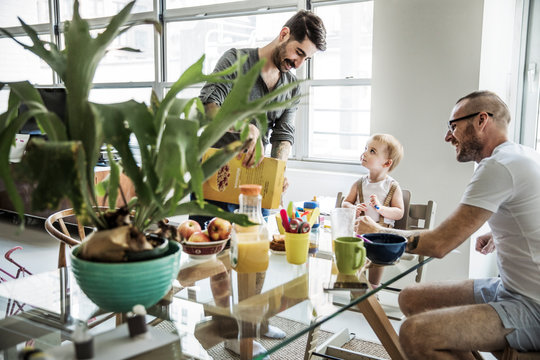 Two fathers and daughter (2-3) having breakfast 