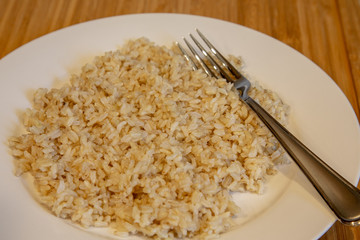 Cooked brown rice on a white plate with fork