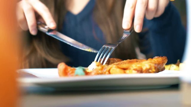 Girl cut a delicious grill chicken meat on a white plate with a knife. Close up 4k food footage.
