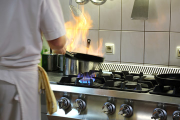 Ogień na patelni w czasie pieczenia, kucharz w kuchni. - obrazy, fototapety, plakaty