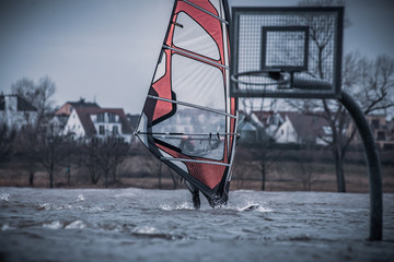 Climate change. High water on the Rhine. Windsurfer surf past basketball hoop.