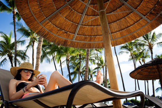 Woman lying on lounge chair under beach umbrella and using mobile phone 