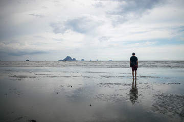 Man walking on the Ao Nang beach from Krabi, Thailand. A beautiful reflection of the sky in the...