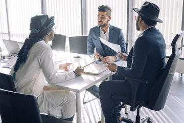 Diverse business partners discussing project sitting at conference table, Arab investor proving his point of view to his european an indian partners and at informal meeting.