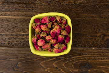 tea rose buds in the clay bowl  isolated on wooden background, top view