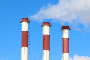 A smoke cloud from three industrial plant chimneys standing in a row against the blue sky